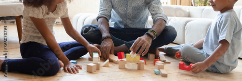 Close up wide banner panorama view of playful african American father with small kids sit on floor play with building bricks, biracial dad with little children construct with wooden blocks at home
