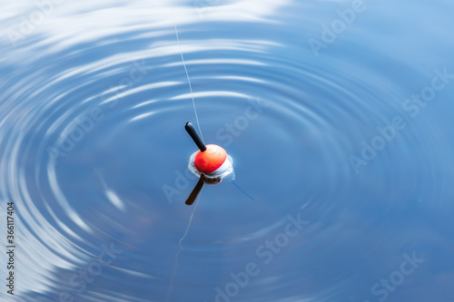 Fishing float in the blue water. A bobber floats on the water surface of the lake making circles in the water. Top view.