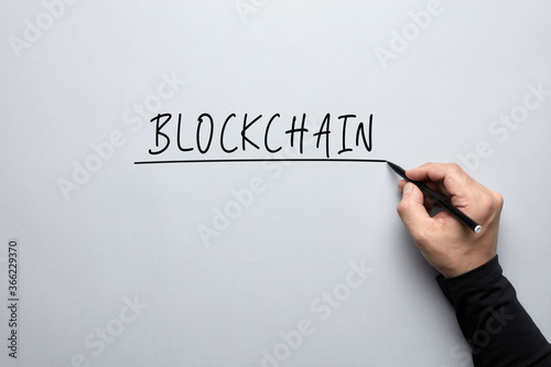 The word blockchain handwritten with a male hand on grey background. Concept of blockchain technology.