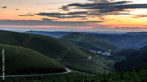Sunset over the south Wales valleys from the Bwlch mountain. A road winds around the hillside to the village of Abergwynfi. The hillside has a wind farm on it. 