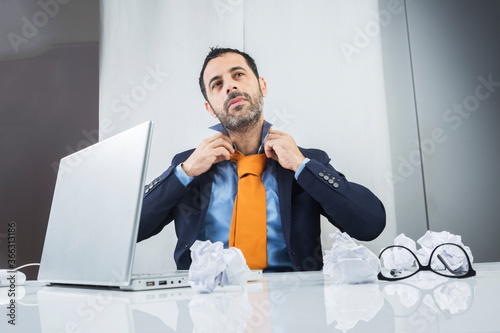 Manager i, giacca e cravatta seduto nella postazione di lavoro del suo ufficio , si aggiusta la cravatta arancione