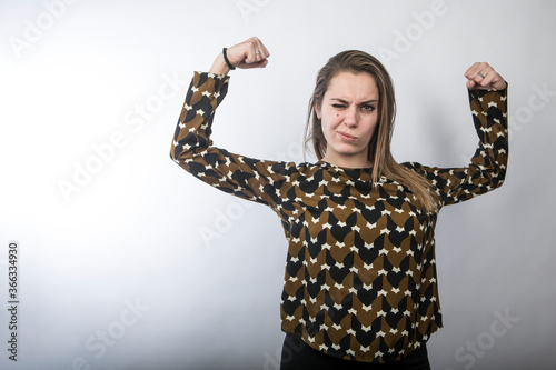 ragazza divertente con maglia fantasia mostra i muscoli delle braccia giocando e facendo la faccia da dura , isolata su sfondo bianco