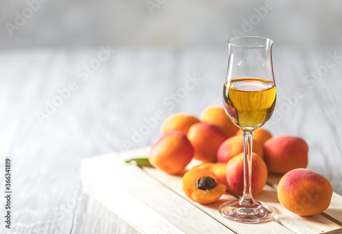 Apricot liqueur in shot glass and fresh apricots on a light wooden table.