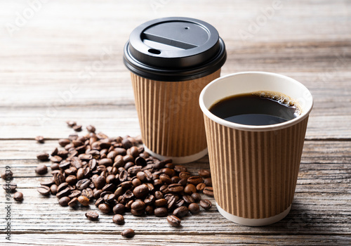 A paper cup of coffee and coffee beans on an old wooden background