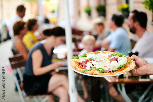 KEllner trägt Pizza zum Gast im Biergarten Terrasse