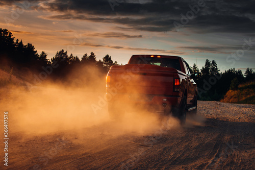 Pickup truck in motion on a country road with clouds of dust. An SUV is driving fast during sunset on a rural gravel road with a lot of dust. fast moving car