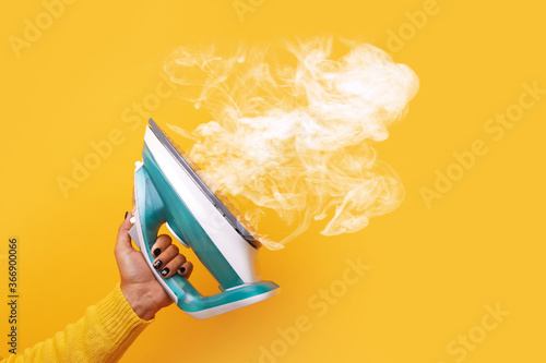 modern iron with steam in hand over yellow background