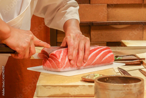 A close-up shot of a sushi chef cutting a chunk of fatty tuna on a cutting board
