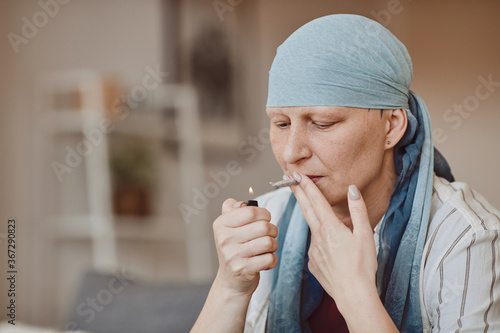 Warm-toned portrait of bald adult woman smoking marijuana for medicinal purposes in cancer recovery, copy space