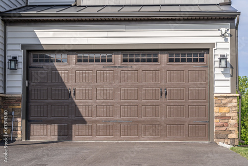 Double car classic insulated steel raised panel brown garage door framed with a white trim to add accent, with transom light windows divided by muntins on a new American home