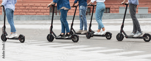 Five friends having ride on motorized kick scooters