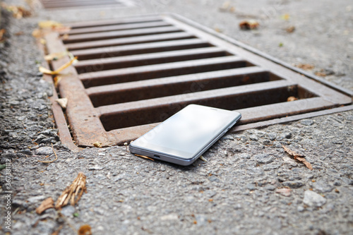 lost smart phone device laying on the ground near rain drain at city street.