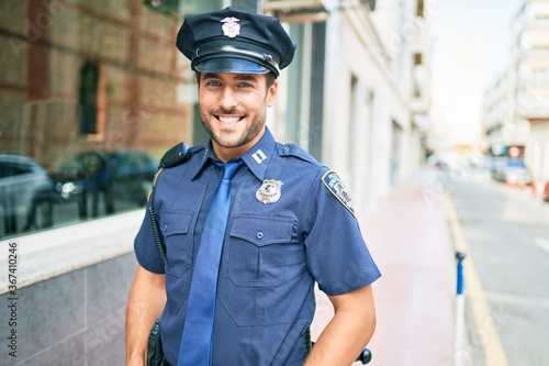 Young handsome hispanic policeman wearing police uniform smiling happy Standing with smile on face at town street.