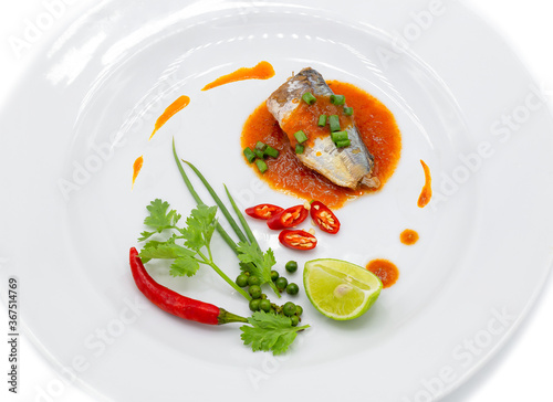 Sardine piece in tomato sauce decorated by chili ,spring onion , pepper , coriander and lemon in the white plate.