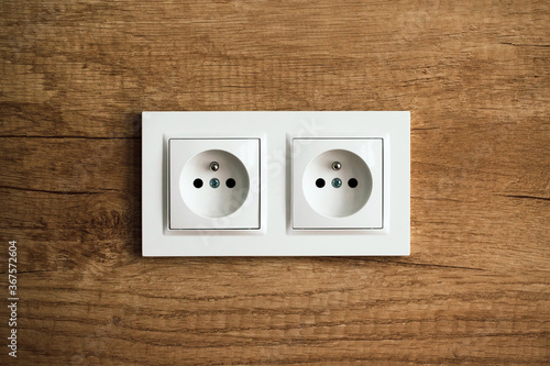 Electrical socket isolated on wooden kitchen wall. Renovated studio apartment power supply background. Empty copy space white plastic double power outlet.