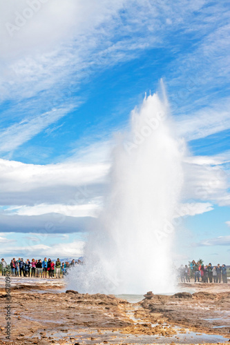 GEYSIR, ICELAND: Eruption of Strokkur geyser, observed by many tourists, on a day with remarkable cloudscape. 
