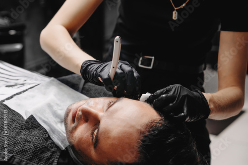 Woman barber shaving a man with a straight razor.