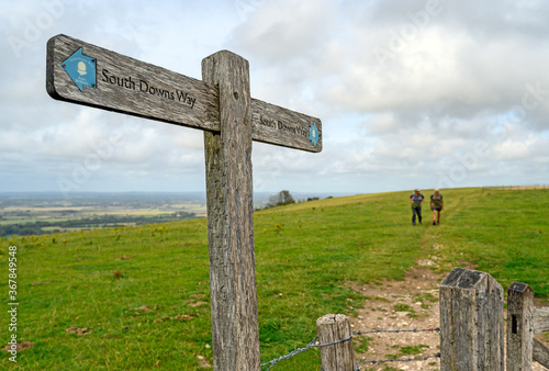 South Downs National Park, Sussex, UK near Firle Beacon. A signpost shows the route of the South Downs Way with two unrecognizable hikers. The South Downs Way is a national trail popular with walkers.