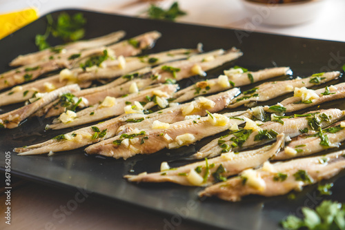 Pickled anchovies with garlic and parsley in a dark plate close-up.