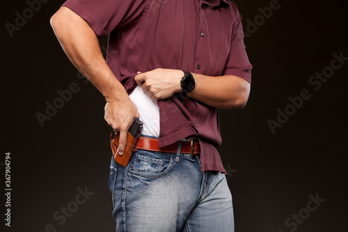 Man lifting up his shirt about to draw his concealed carry pistol from his holster.