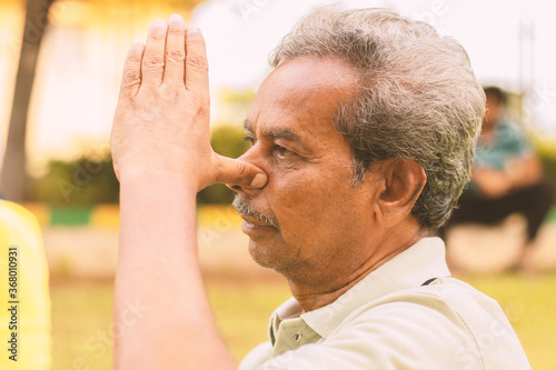 Closeup of of senior man doing alternate Nostril Breathing exercise or nadi shodhana pranayama at park - Concept of healthy active old people lifestyle.