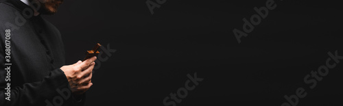 panoramic orientation of priest holding wooden cross isolated on black
