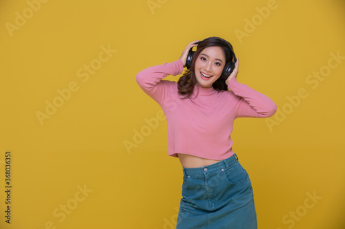 smiling and Happy cheerful Beautiful Asian woman wearing wireless headphones enjoying listening to music on yellow background.People lifestyle concept