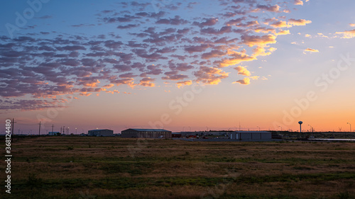 Colorful dark dawn sunrise in Snyder Texas with industrial building, warehouses or storehouses and factory by farm field with electricity pylons