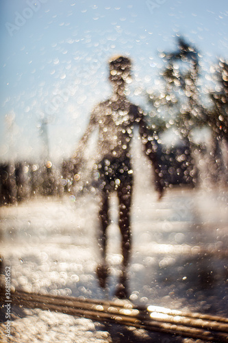 The silhouette of a boy is seen behind the drops of water in the fountain