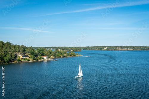 Amazing panorama of blue Baltic sea bay. View from the top of cruise ship. Rocky shores of Scandinavia at summer day. White sailing yacht moving along beautiful forest pine islands. 