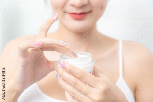 A woman holds a moisturizer in her hand and her skin and wrinkle from impurities.