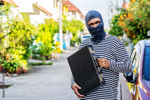 The male thief wears a black and white striped shirt and wears a black mask, smiling happily after stealing briefcase with money he wants.