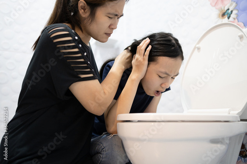 Sick asian child girl about to throw up,puking,vomiting into the toilet bowl,mother is taking care of her closely,suffering from indigestion,food poisoning,acute infectious diseases,gastritis problem