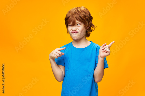 Red hair blue T-shirt yellow background boy shows the direction 