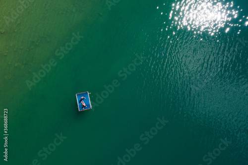 Floating platform with a sun tanning couple aerial top view. Bright sn reflecting in green lake waves. Peruca Lake, Dalmatia, Croatia