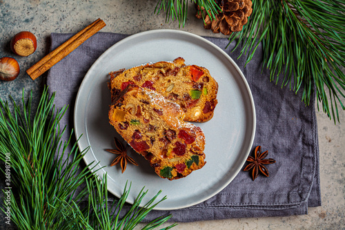 Pieces of Christmas fruit cake on plate in festive decorations, top view, dark background.