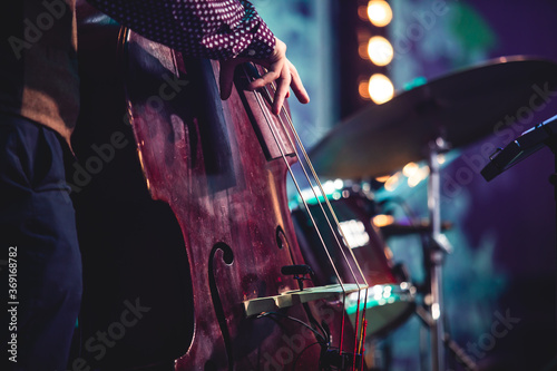 Concert view of a contrabass violoncello player with vocalist and musical during jazz orchestra band performing music, violoncellist cello player on stage