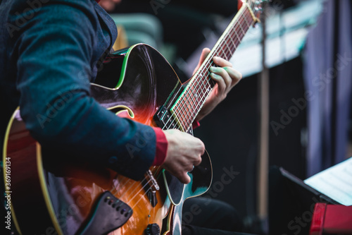 Concert view of an electric acoustic guitar player with vocalist and musical jazz band orchestra performing in the background, guitarist on the stage