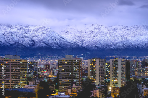 Panorama of amazing purple cloudy sky over Santiago skyline and the snowed Los Andes mountains at the nightfall, Chile