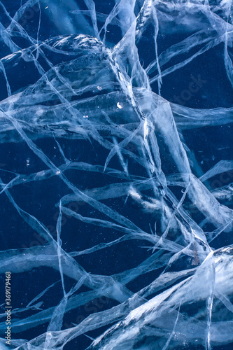 A grid of cracks in blue clear ice. Beautiful pattern on transparent ice. Vertical.