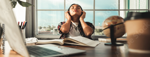 Asian young woman or female student sitting at table relax with her headphones after learning through online lessons at home. Closed eyes feels satisfaction after finish learning. Education from home.