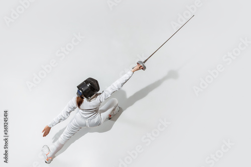 Champion. Teen girl in fencing costume with sword in hand on white background. Top view. Young female model practicing and training in motion, action. Copyspace. Sport, youth, healthy lifestyle.