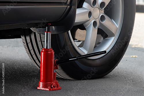 The red hydraulic bottle jack is installed under the machine and lifting it.