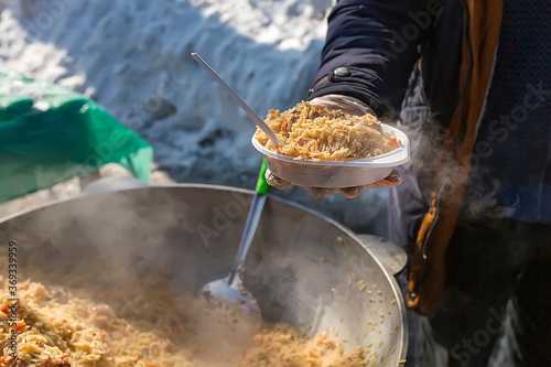 Cook cooks pilaf in a cauldron. A man interferes with rice.