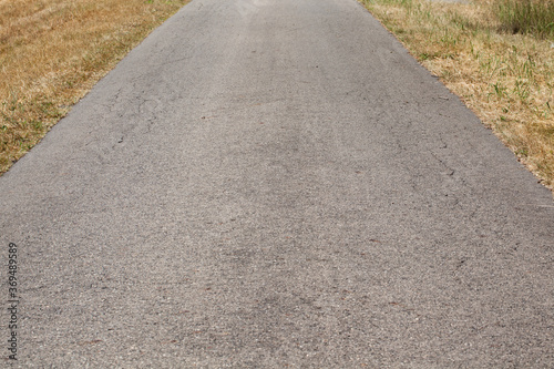 Wąska asfaltowa droga na wsi wraz z trawiastym poboczem spalonym od słońca.