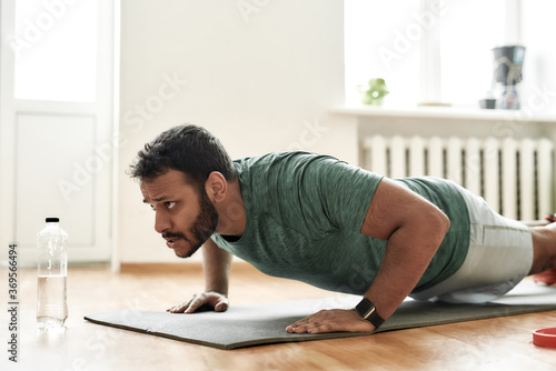 Fight for fit body. Young active man looking focused, exercising, doing push ups during morning workout at home. Sport, healthy lifestyle