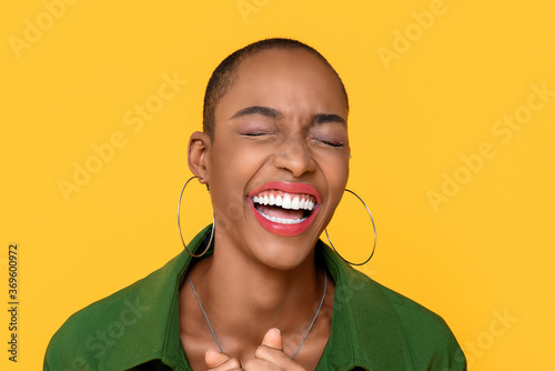 Close up portrait of happy African American woman laughing with eyes closed in isolated studio yellow background