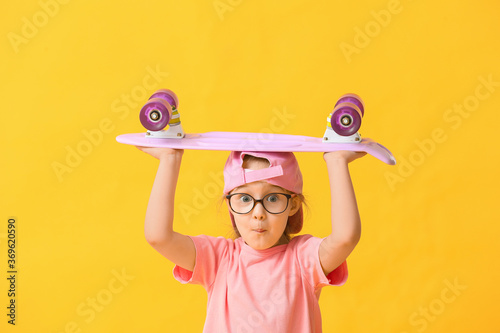 Cute little girl with skateboard on color background