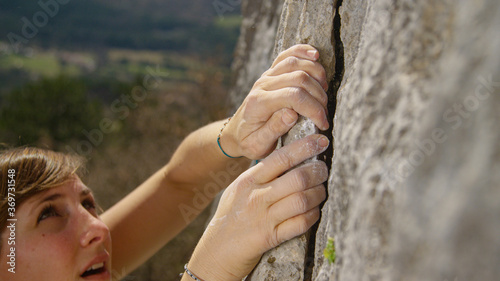 CLOSE UP: Fit female lead climber holds on to a flake grip on a massive cliff.