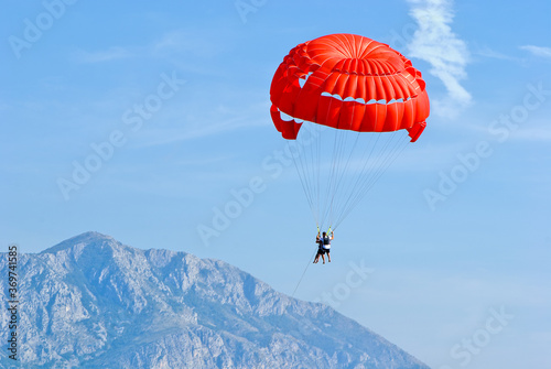 Tandem, two persons flying on a red parachute on sky background